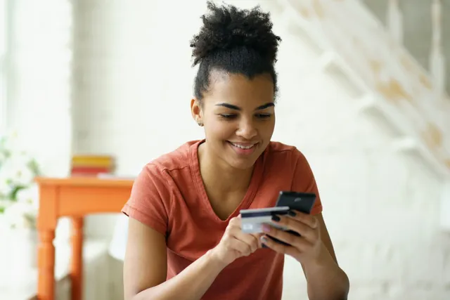 A customer smiling while paying online with a phone and a bank card