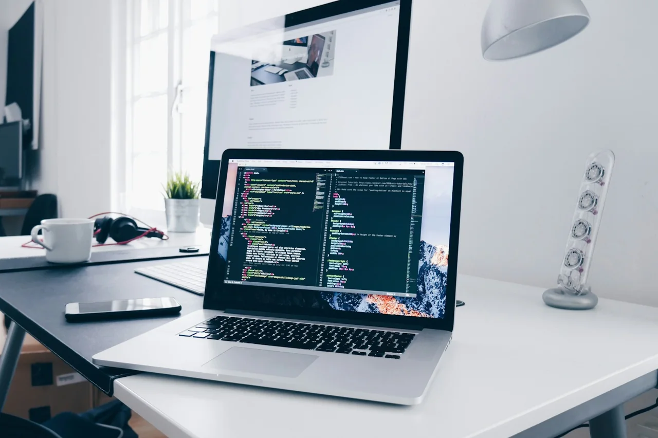 Laptop displaying source code beside a desktop monitor in a bright workspace